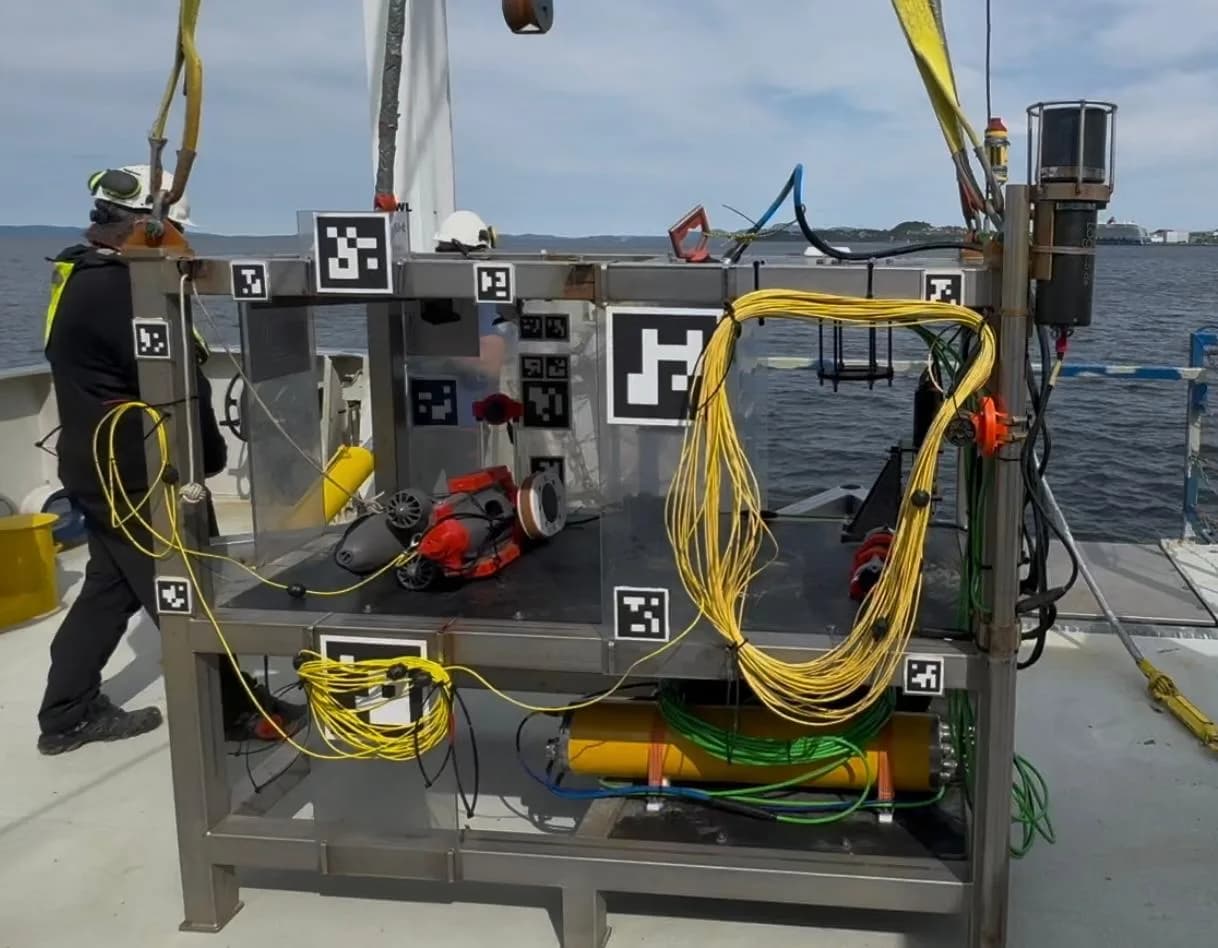 Estructura metálica de docking con muchos marcadores ArUco y un pequeño ROV dentro, sobre la cubierta de un barco
